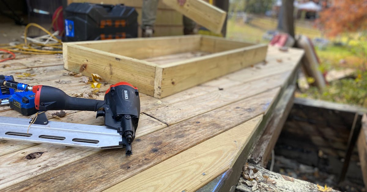 Close-up of carpentry work on a deck with a nail gun and wooden frame under construction.