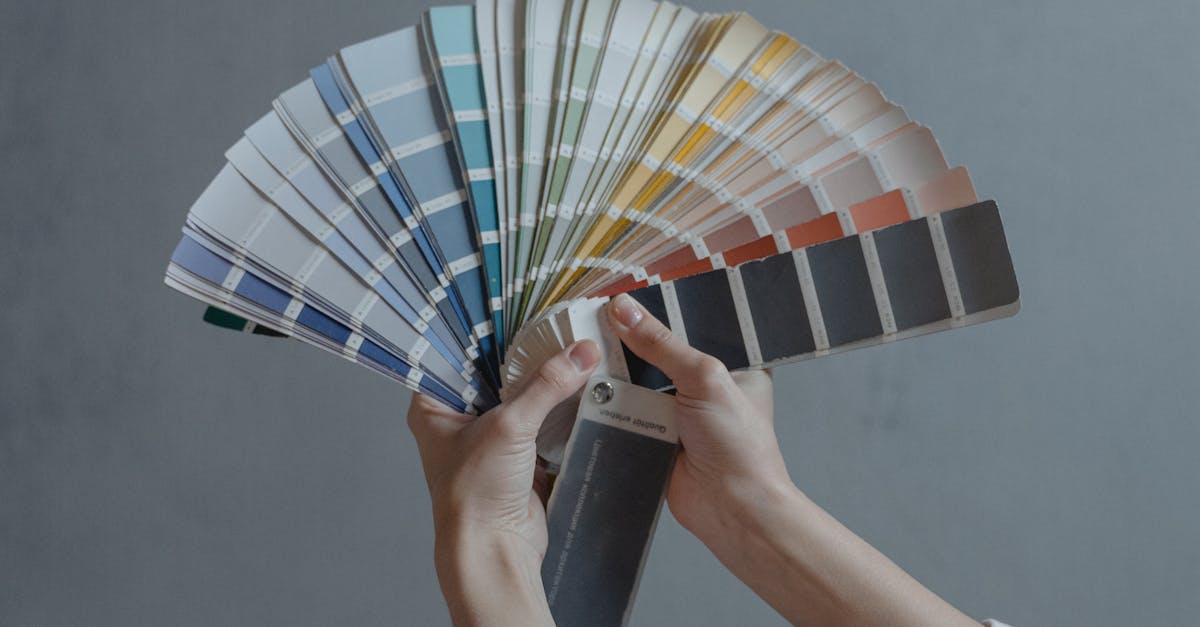 Hands displaying a fan of paint color swatches against a gray wall, ideal for home renovation projects.